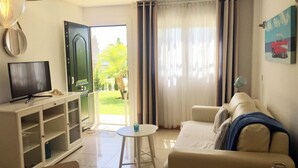 A living room with a TV, a sofa, a small table, and a door leading to an outdoor area.