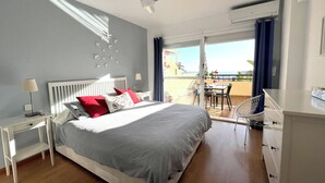 A bedroom with a bed, bedside tables, a dresser, and a balcony with a table and chairs.