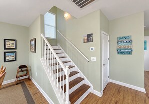A staircase with white railings and wooden steps, a wall with framed pictures, and a decorative sign with beach-related words.