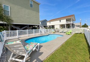 A backyard with a swimming pool, a covered patio, and a white fence.