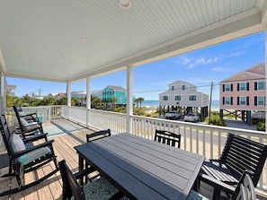 A covered outdoor deck with a table and chairs, overlooking a beach with colorful houses.