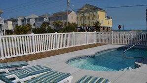 A swimming pool with lounge chairs, a white fence, and a view of buildings in the background. - Billy-Lisa - Second Row in Garden City Beach, SC (Garden City)