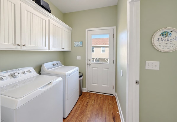 A laundry room with a washer and dryer, a white door, and a wall with a decorative plate. - Billy-Lisa - Second Row in Garden City Beach, SC (Garden City)