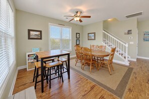 A dining area with a wooden table and chairs, a ceiling fan, and a staircase leading upstairs.
