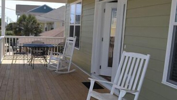 A covered porch with a table and chairs, a rocking chair, and a door leading to the house. - Billy-Lisa - Second Row in Garden City Beach, SC (Garden City)