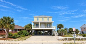A two-story house with a balcony, a covered walkway, and a beach view.