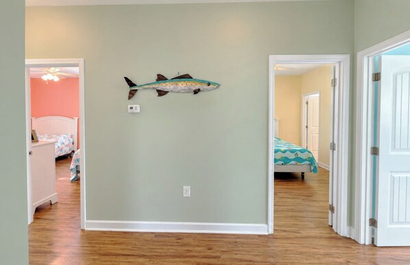 A hallway with a fish wall art, a ceiling fan, and a bed with a patterned bedspread.