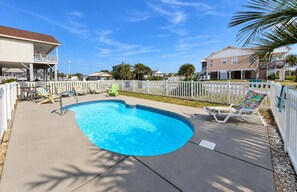 A residential swimming pool with a curved edge, surrounded by a white fence, and equipped with lounge chairs. - Billy-Lisa - Second Row in Garden City Beach, SC (Garden City)
