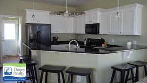 A kitchen with white cabinets, a black refrigerator, and a central island with stools. - Billy-Lisa - Second Row in Garden City Beach, SC (Garden City)
