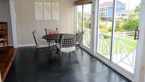 A dining area with a round table and chairs, a ceiling fan, and a view of a house through a large window. - Swamp Fox (Formerly Footprints) - Second Row in Garden City Beach, SC (Garden City)