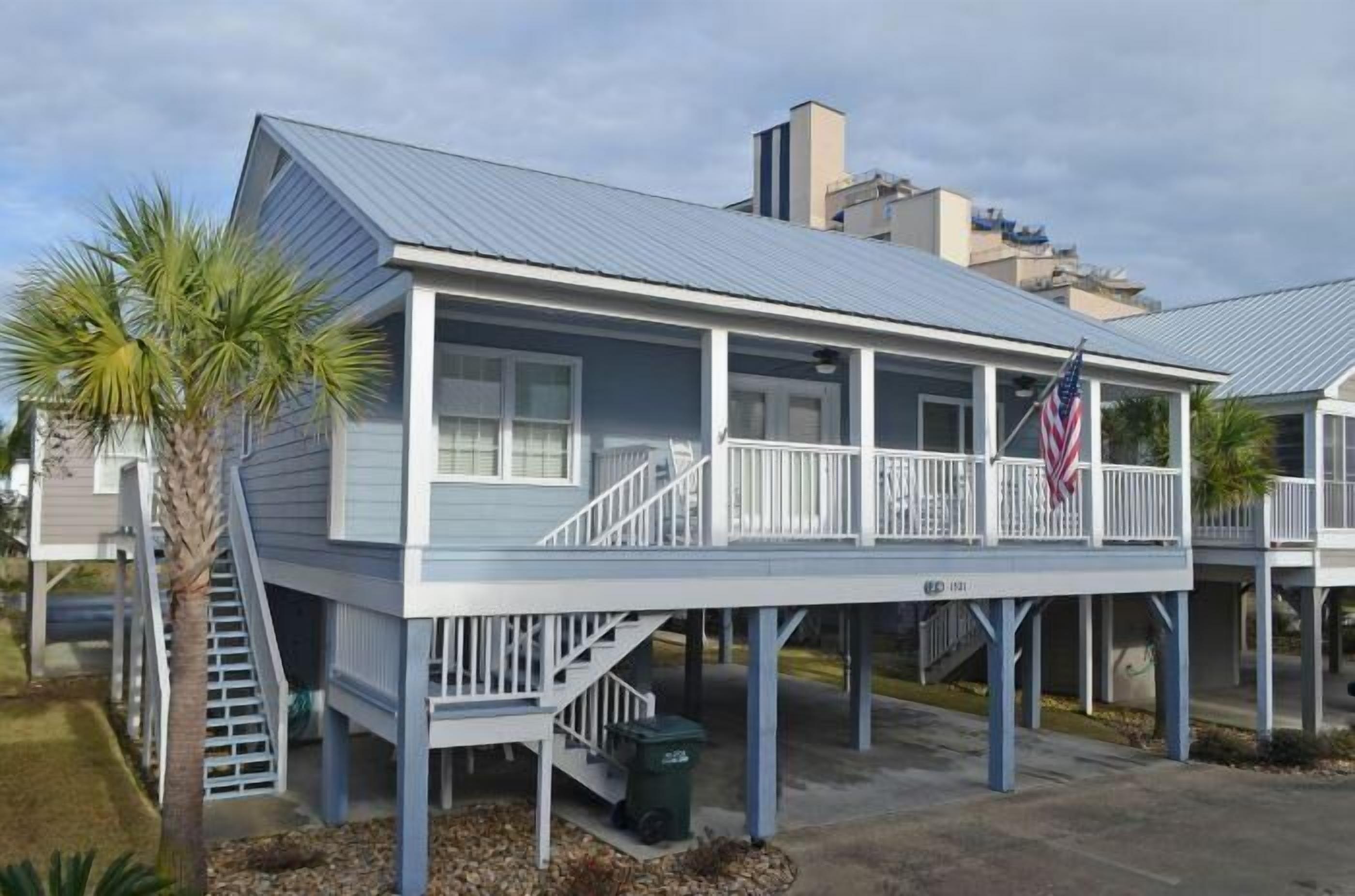 Ein Küstenhaus mit überdachter Veranda, einer Treppe und einer amerikanischen Flagge.