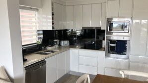 Una cocina moderna con armarios blancos, microondas integrado, lavavajillas y una mesa de comedor de madera.