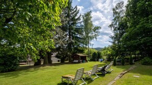 Nurmikkoalue ulkona, jossa on aurinkotuoleja ja taustalla pieni rakennus.