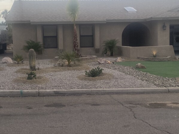 Un edificio con techo plano, una entrada abovedada amplia y un jardín ajardinado con cactus y arbustos pequeños.