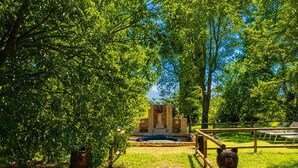 A pathway leading to a fountain surrounded by trees and a wooden fence.