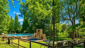 A pool area with a stone fountain, wooden lounge chairs, and a wooden fence.