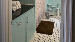 A bathroom with a black countertop, a patterned shower curtain, and a small stool.