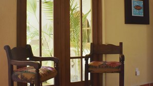 Une pièce avec deux chaises en bois, un sol carrelé, une porte avec des panneaux de verre et un luminaire fixé au mur.