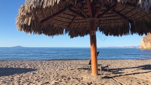 Une plage avec un parasol en chaume et une chaise longue.