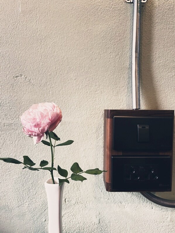 A pink rose in a white vase against a textured wall with a black electrical box mounted on it. - Peaceful Homestay and Camping at KhaoKho (Khao Kho)