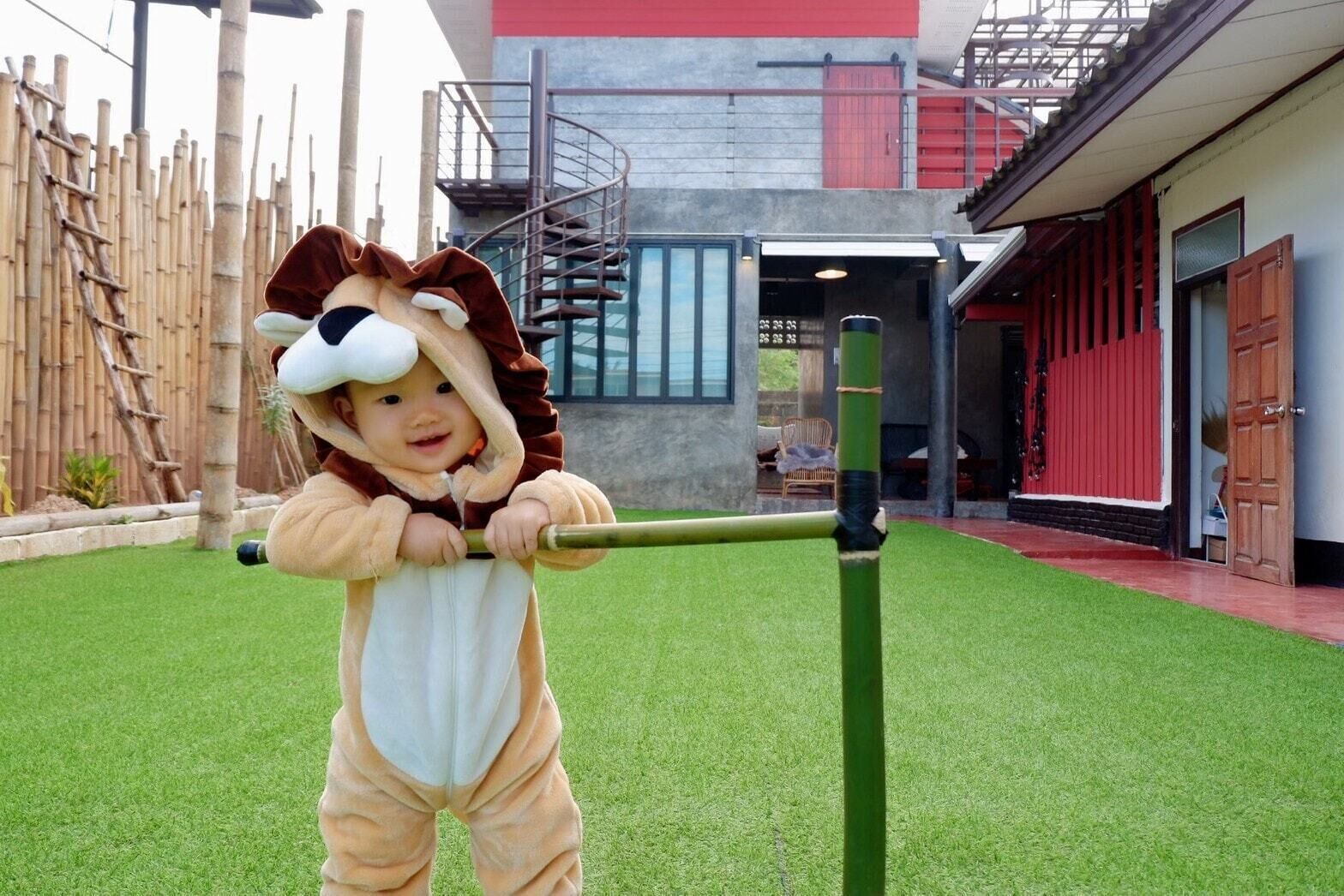 A child in a lion costume playing on a green artificial grass field with a modern building in the background.