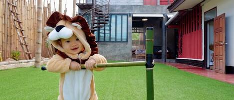 A child in a lion costume playing on a green artificial grass field with a modern building in the background.