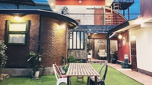 A patio area with a wooden table and chairs, surrounded by a brick wall and a small garden.