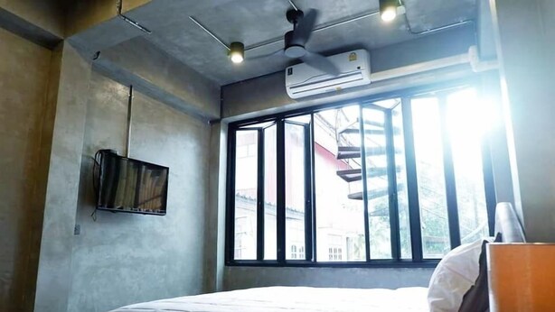 A bedroom with a bed, a ceiling fan, an air conditioner, a window with bars, and a wall-mounted TV.