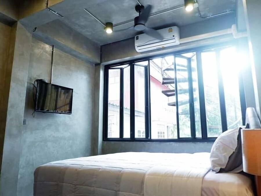 A bedroom with a bed, a ceiling fan, an air conditioner, a window with bars, and a wall-mounted TV.