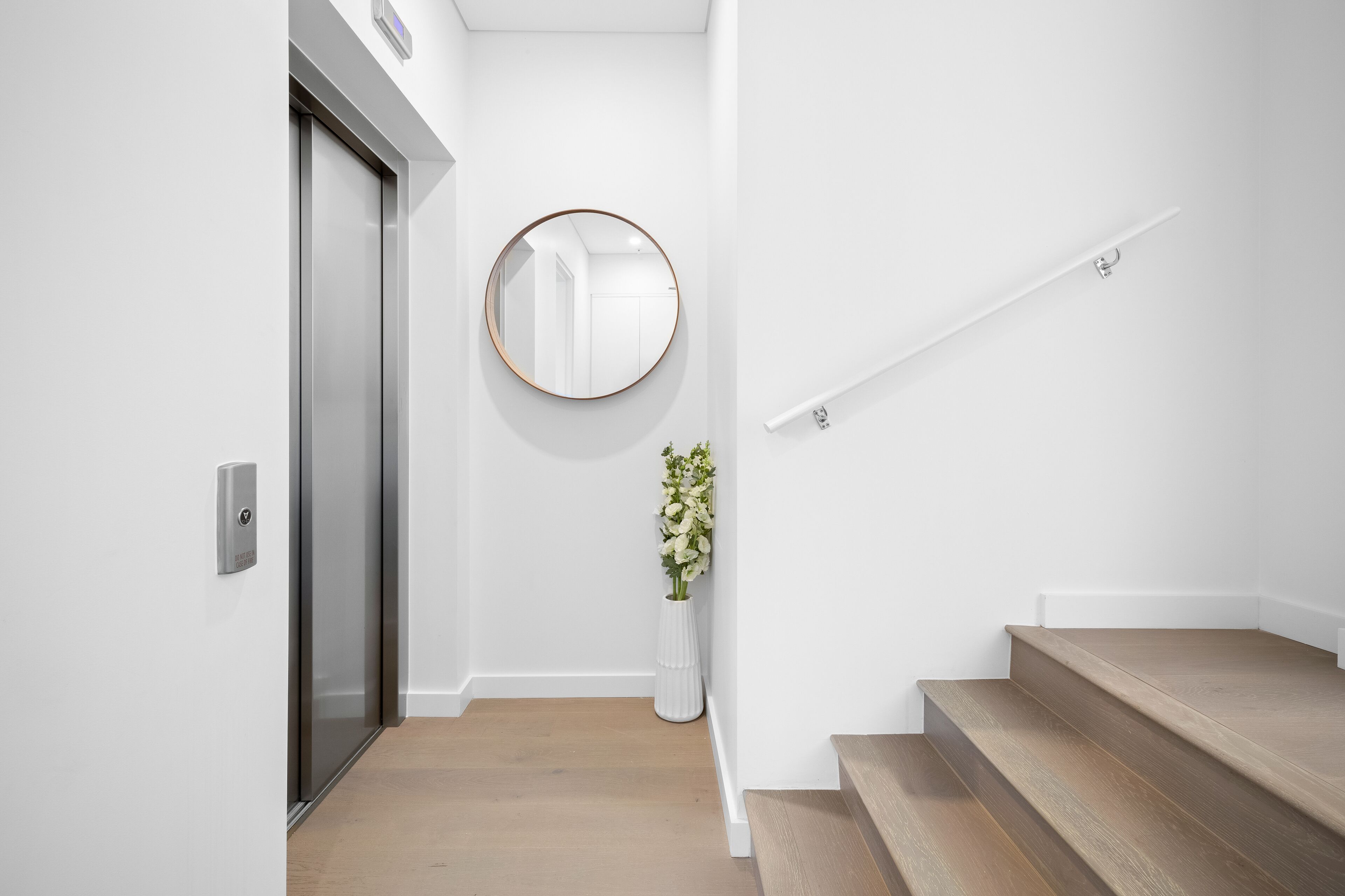 A modern interior with a wooden staircase, a round mirror, and a white wall.
