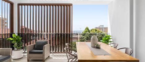 A modern balcony with a wooden table and chairs, potted plants, and a view of the cityscape.