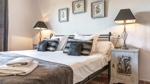 Ein ordentlich bezogenes Bett mit Kissen, ein Nachttisch mit Lampe und gerahmte Bilder an der Wand.