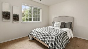 Ein Schlafzimmer mit großem Fenster, einem Bett mit gemustertem Überwurf und zwei an der Wand hängenden Bildern.