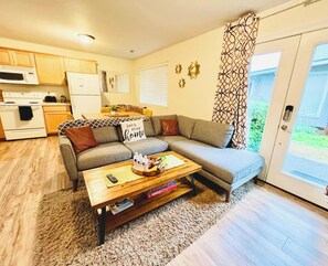 A compact living space with a sofa, coffee table, and kitchen area including a microwave and refrigerator.