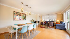 A modern living room with a dining area, a fireplace, and a large window with blinds. - Peaceful Seafront Location – Casa Es Pí (Llucmajor)