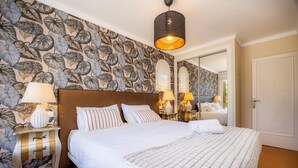 A neatly made bed with white linens, a patterned wall, and a mirror reflecting the room. - Peaceful Seafront Location – Casa Es Pí (Llucmajor)