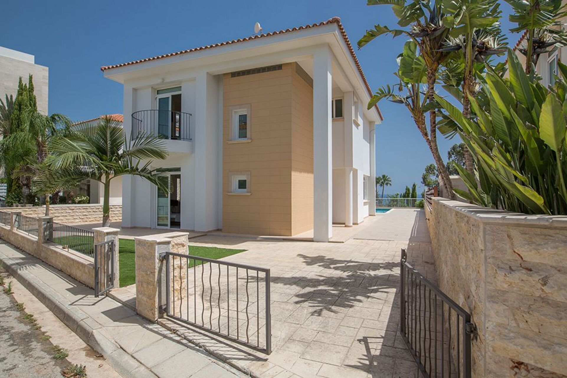 A modern two-story residential building with a balcony, a swimming pool, and a stone wall.
