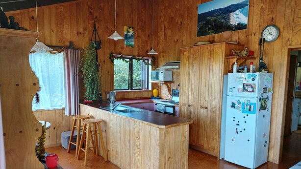 A wooden-paneled kitchen with a central island, bar stools, a refrigerator, and a microwave.