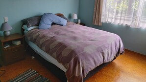 A bedroom with a bed, pillows, a nightstand, a lamp, and a window with curtains.