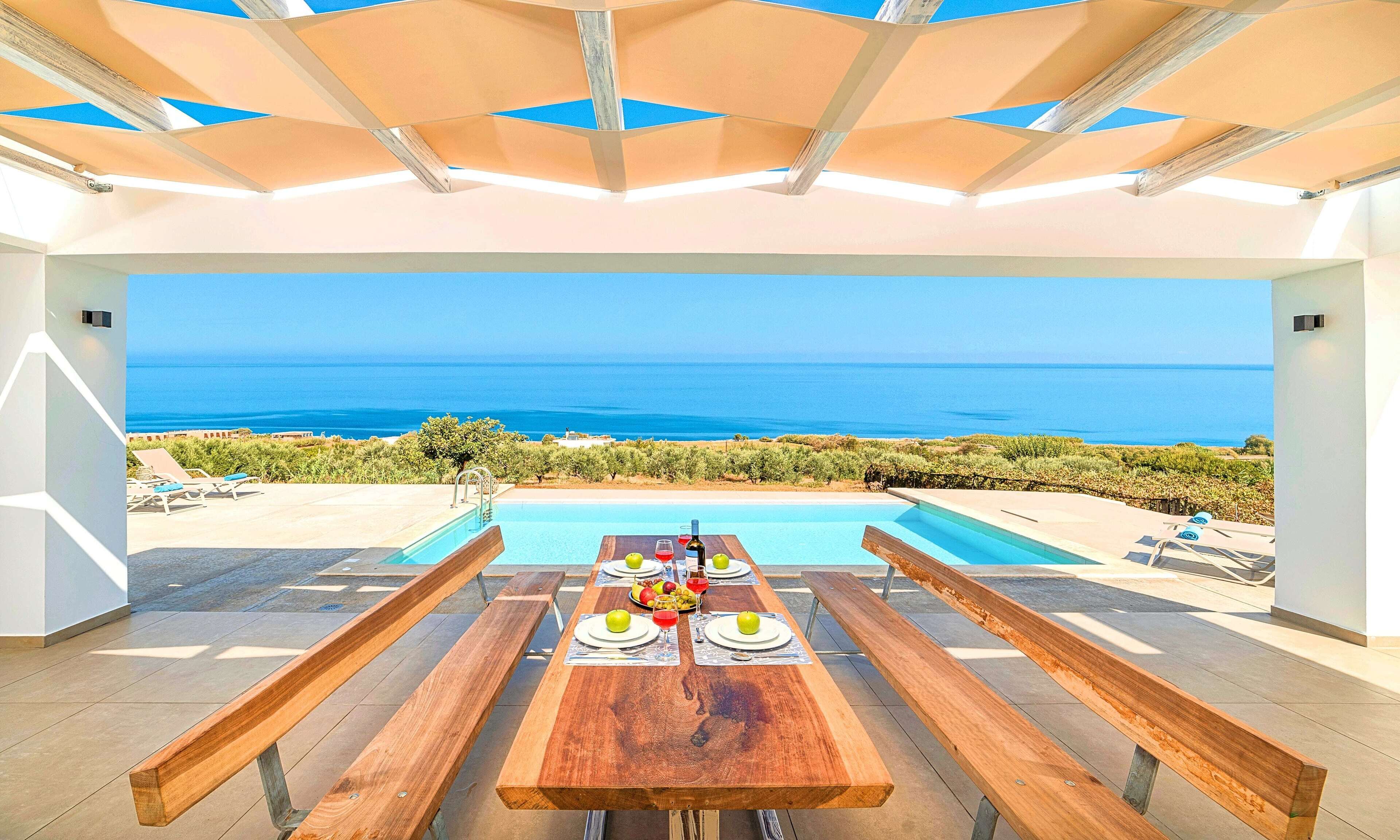 Un espace repas offrant une vue sur la mer, une piscine, et une table mise avec des assiettes, des verres et une bouteille.