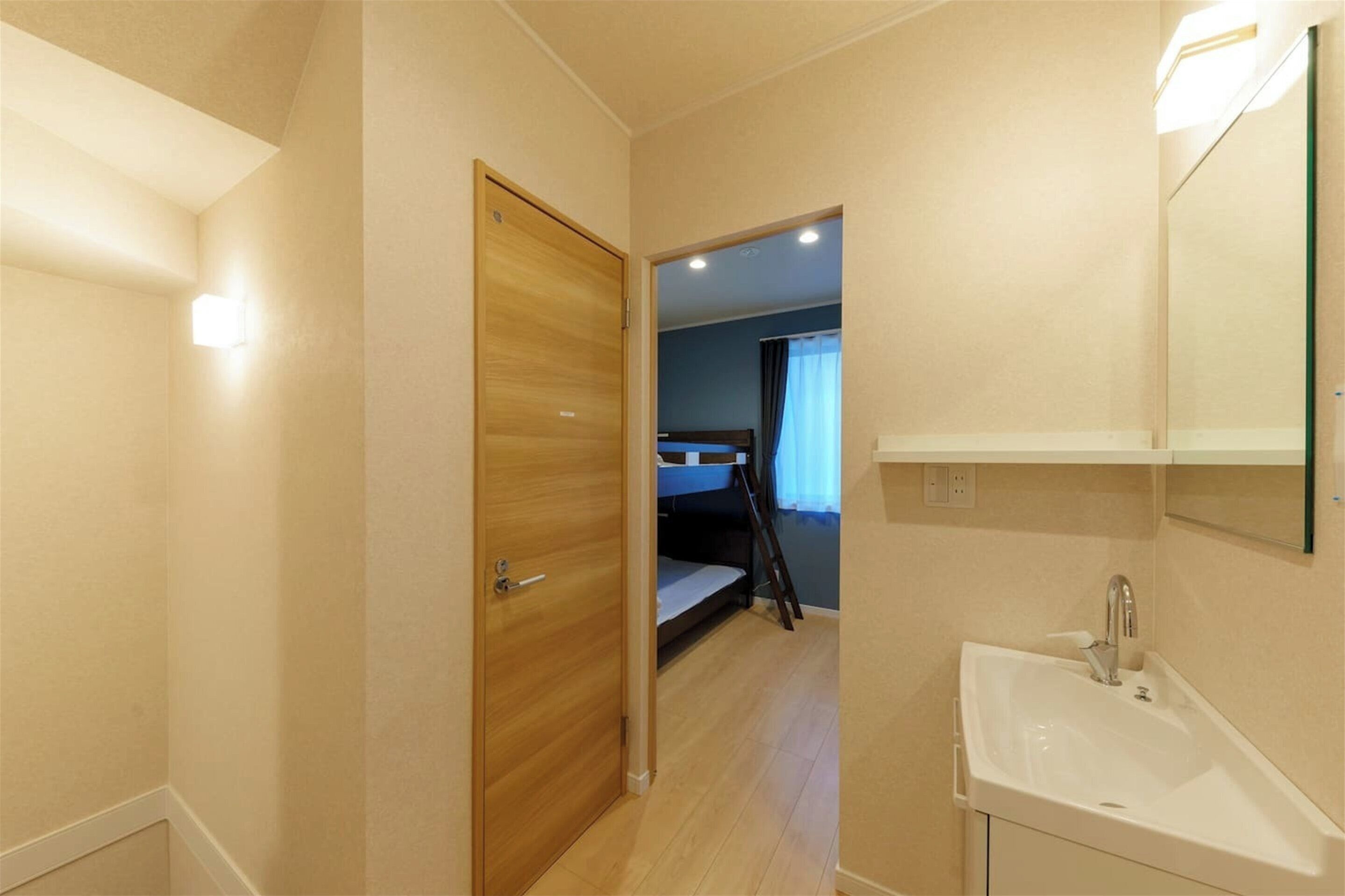 A small, well-lit room with a wooden door, a bunk bed, a white sink, and a mirror.