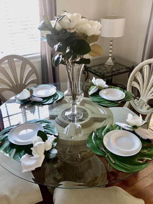 A dining table set with white plates, silverware, and a vase with white flowers.