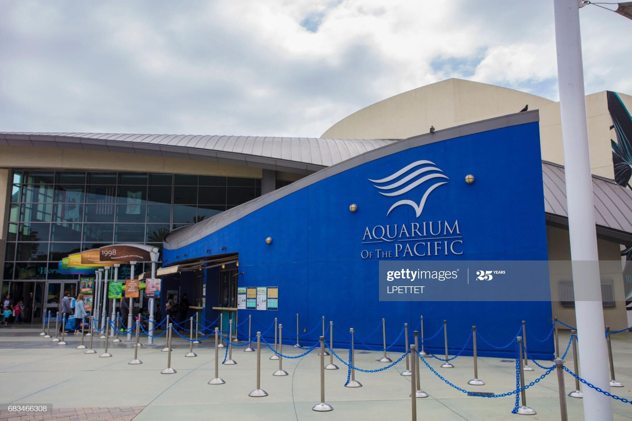 Das Außengebäude des Aquarium of the Pacific mit blauer Fassade, Glastür und einer Kettenbarriere davor.