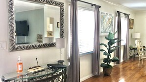 A room with a glass-top console table, a large ornate mirror, a potted plant, and a window with curtains. - Cozy Condo in Downtown Long Beach, 2 min walk to the Beach,parking place+garage  (Long Beach)