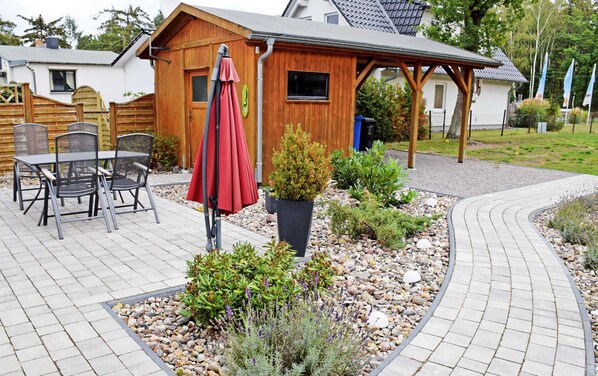 Uma cabana de madeira com um terraço que inclui móveis de exterior e um guarda-sol vermelho.