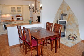Uma cozinha com armários de madeira, uma ilha central com cadeiras, um candelabro e uma lareira de pedra.