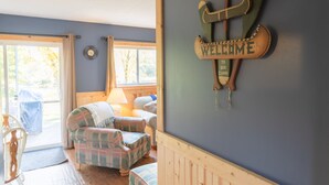 A cozy room with a plaid sofa, a wooden welcome sign, and a lamp. - Cozy Riverfront Cottage (Hersey)
