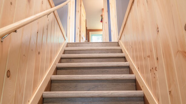 A wooden staircase with a handrail, leading to a room with a door at the top. - Cozy Riverfront Cottage (Hersey)
