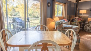 A dining area with a wooden table and chairs, a sofa, and a fan. - Cozy Riverfront Cottage (Hersey)