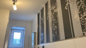 A bathroom with a shower, a window, and decorative wall panels.